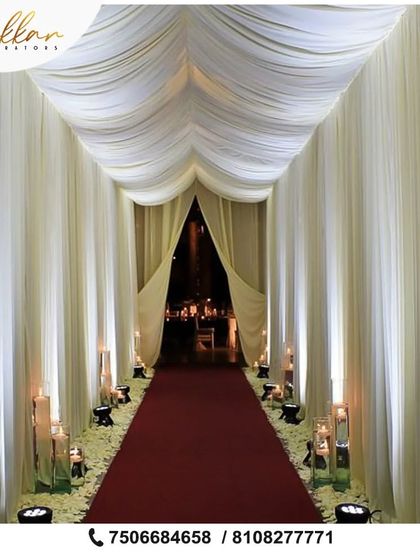 A simple yet incredibly elegant entrance. I used flowing white drapes to create a tunnel effect, with a red carpet and large candles lining the path for a dramatic and sophisticated welcome.