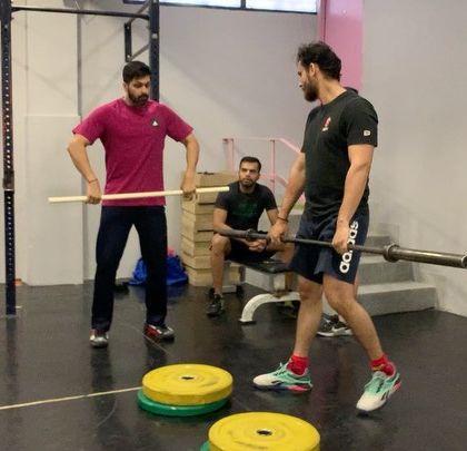 Technique first. A coach uses a light bar to correct an athlete's form during a weightlifting seminar, ensuring proper movement patterns are established early on.
