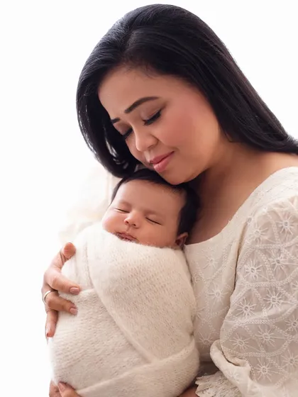 A serene portrait of Bharti Singh holding her sleeping newborn son, Laksh. The all-white theme creates a pure and peaceful feeling.