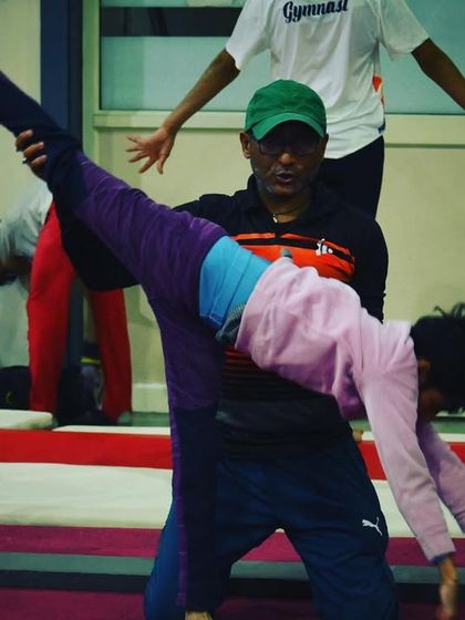 A coach assists a student with a walkover on the beam, demonstrating our hands-on approach to teaching complex skills.