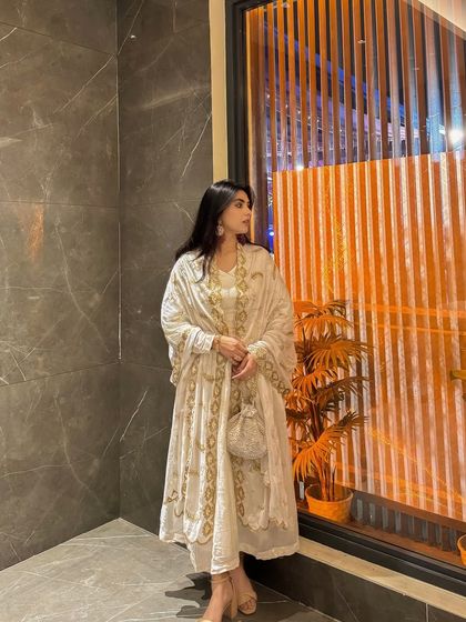 A side profile of the white and gold Anarkali, highlighting the flow of the fabric and the intricate embroidery along the edges.