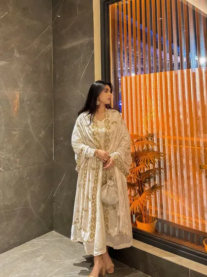 A side profile of the white and gold Anarkali, highlighting the flow of the fabric and the intricate embroidery along the edges.