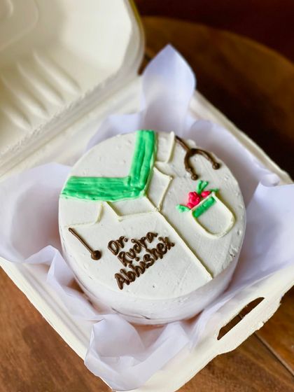 A thoughtful cake for a doctor, Dr. Kyra Abhishek. The design includes a doctor's coat, a stethoscope, and a small bouquet of flowers, making it a perfect professional milestone cake.