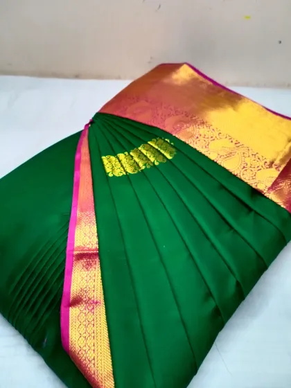 A deep green saree with a bright yellow and pink border, pleated for a special day. The crisp folds ensure the colors pop and the drape is perfect.