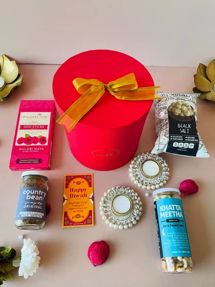 My round box hampers are a popular choice. This red one is filled with snacks, incense, and pearl T-light holders, making it a delightful and affordable Diwali gift.