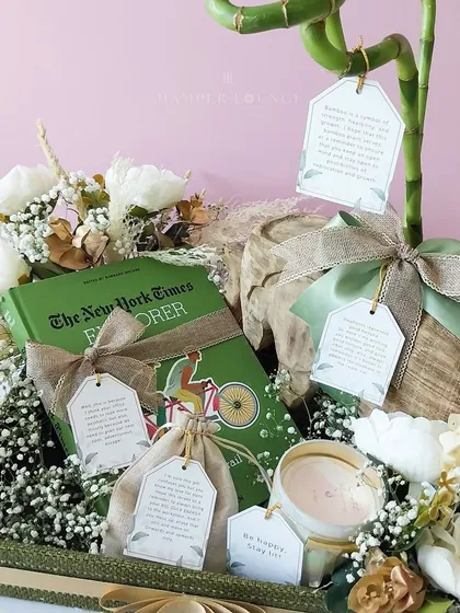 A close-up of the sustainable hamper, highlighting the book "The New York Times Explorer" and other curated items with personalized tags. Each element is chosen to inspire and delight.