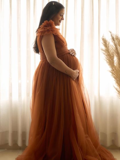 A silhouette shot of the Copper gown. The flowing tulle fabric is beautifully backlit, highlighting the shape of the baby bump.