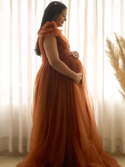 A silhouette shot of the Copper gown. The flowing tulle fabric is beautifully backlit, highlighting the shape of the baby bump.