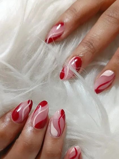 Another angle of the red and pink abstract wave design on almond-shaped nails.
