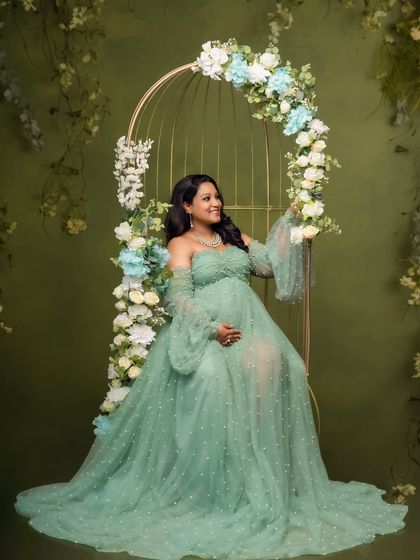 Seated like a queen on a floral-adorned birdcage chair, this mom-to-be looks serene in her flowing green gown.