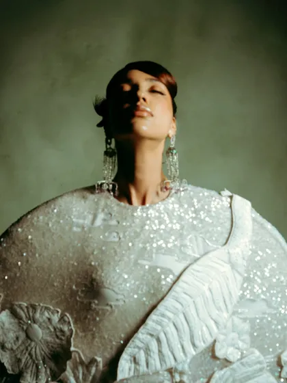 A beauty-focused shot highlighting the sequined texture and floral appliqué of a Rahul Mishra garment. The soft lighting and upward gaze create a serene and ethereal mood.