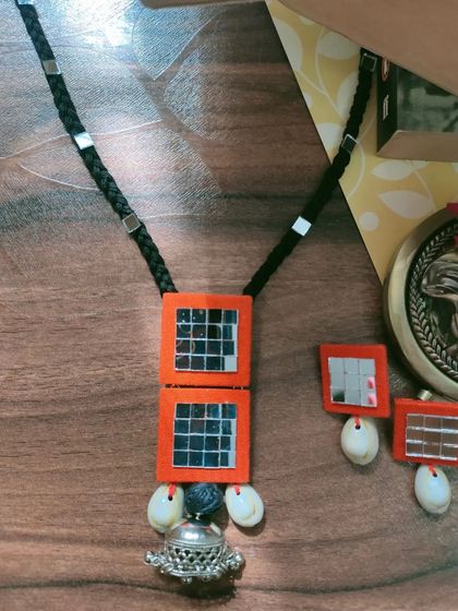A complete view of this handmade Navratri necklace set. It features bright orange fabric squares with intricate mirror work, cowrie shell accents, and a large oxidized silver jhumka pendant.