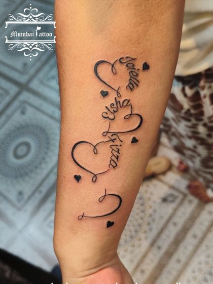 A beautiful family tattoo weaving the names "Joella," "Elsha," and "Fiza" into a series of interconnected hearts. This is a creative way to represent the bond between loved ones.