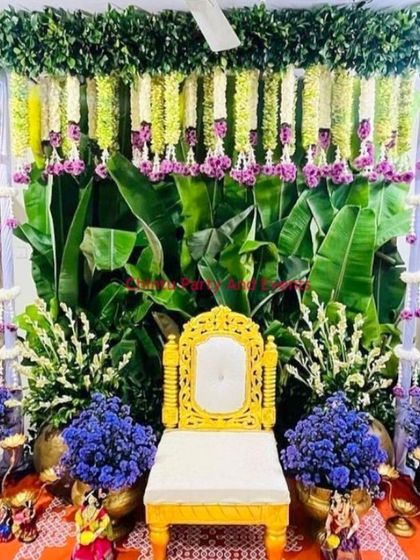 An elaborate traditional baby shower (Seemantham) setup. The decor features a banana leaf wall, hanging flower garlands, and large bouquets of blue flowers.
