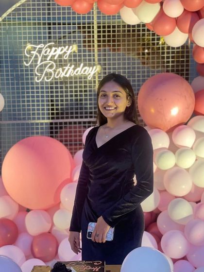 The birthday girl posing in front of her beautiful pink and white balloon wall, a perfect backdrop for memorable photos.