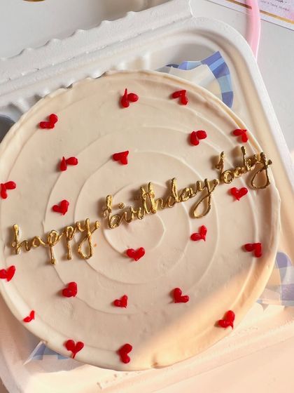 A close-up view of the delicate gold lettering on a white buttercream bento cake. The combination of gold script and red hearts creates a classic, celebratory feel.