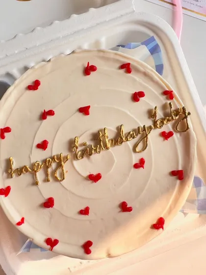 A close-up view of the delicate gold lettering on a white buttercream bento cake. The combination of gold script and red hearts creates a classic, celebratory feel.