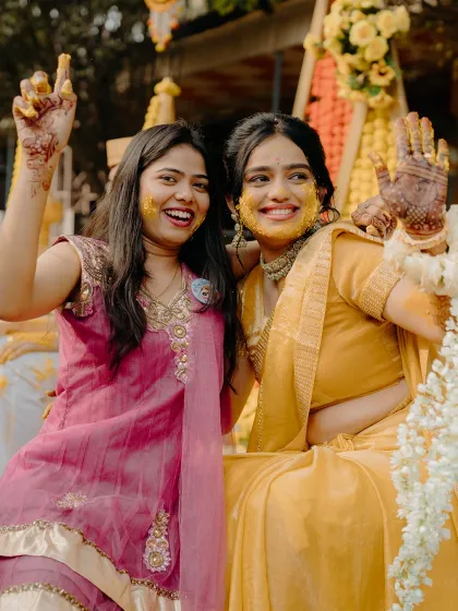 Sisters and friends celebrating together during the Haldi. The genuine smiles and turmeric-smeared hands show the fun and messy reality of this ceremony.