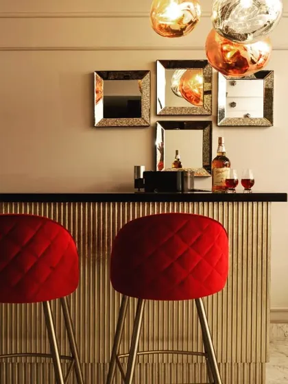 A close-up of the bar area, featuring bold red quilted stools that add a pop of color and glamour. The metallic finish on the bar and the cluster of pendant lights create a chic, festive mood perfect for entertaining.