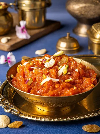 A warm and inviting bowl of Gajar Halwa. The brass bowl and blue background create a beautiful contrast, making the orange of the carrots look even more vibrant and delicious.
