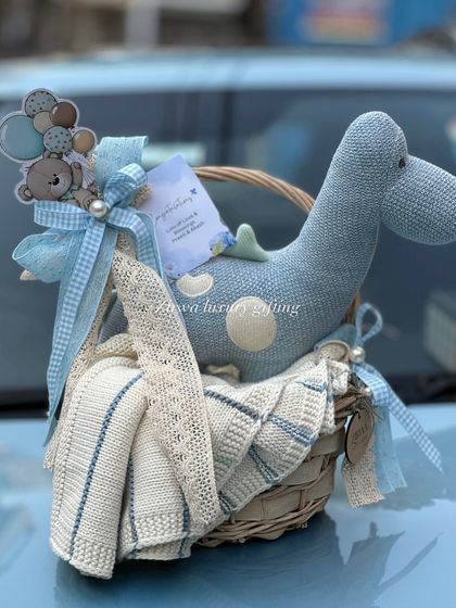 Another look at the aesthetic mini basket for a baby boy. The combination of the knitted dinosaur, soft blanket, and coordinated blue ribbons makes it a simple yet elegant gift.