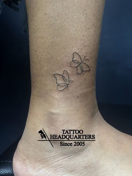 Two minimalist, fine-line butterflies tattooed on the ankle, a delicate and popular choice.