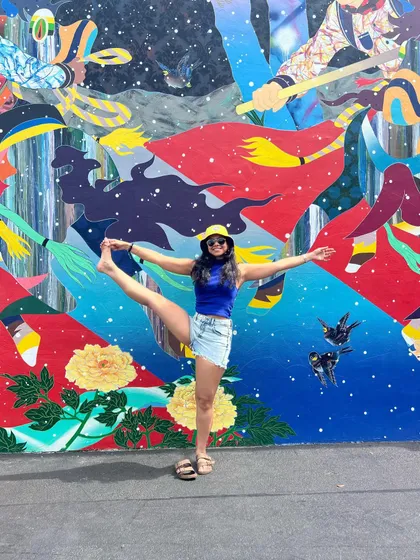 The show must go on. A fun, playful yoga pose against a vibrant mural, embracing the energy of summer.