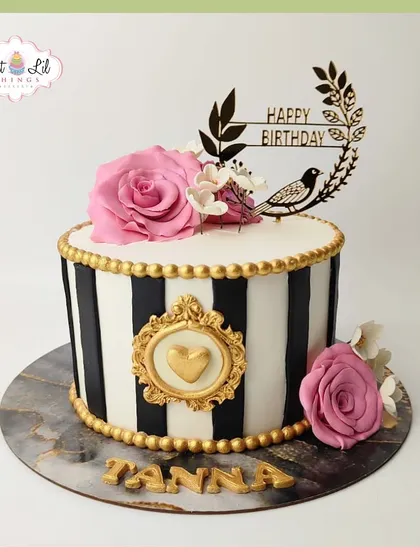 A chic and stylish birthday cake for Tanna, featuring black and white stripes, gold accents, and beautiful pink roses.
