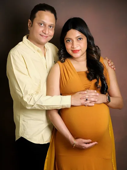 A simple and sweet studio portrait. The couple is dressed in complementary warm tones that match the mustard yellow gown, creating a cohesive and polished look against a classic brown backdrop.