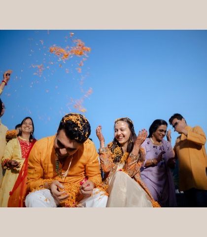 The couple laughing as they are showered with flower petals. A candid moment of pure happiness from their outdoor Haldi ceremony.