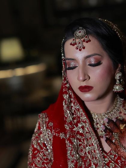 A close-up portrait of a bride with stunning glittery red eyeshadow and a bold red lip. Her smile shows her happiness with the final look.