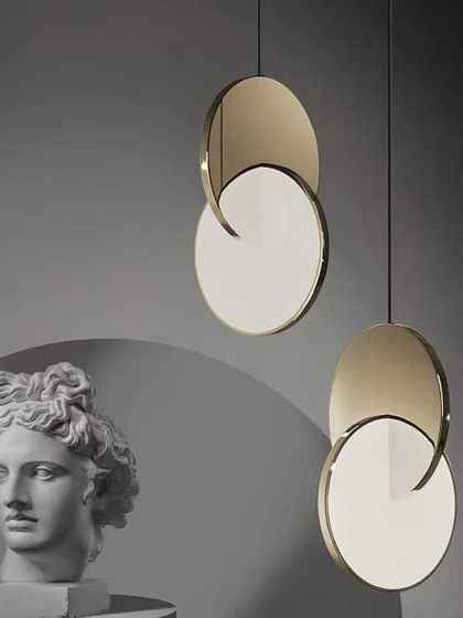 A pair of minimalist pendants with overlapping metal discs. This design plays with light and shadow, creating a subtle eclipse effect.