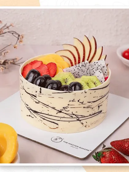 A beautiful example of our fresh fruit cake, topped with an artful arrangement of sliced apples, strawberries, kiwi, mango, and grapes, all surrounded by a modern chocolate-splashed border.