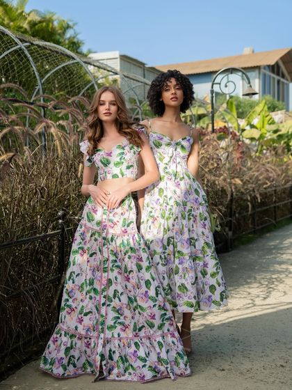 An outdoor shot for Tangerine Tiger, with two models in long floral dresses, creating a romantic, garden-party aesthetic.