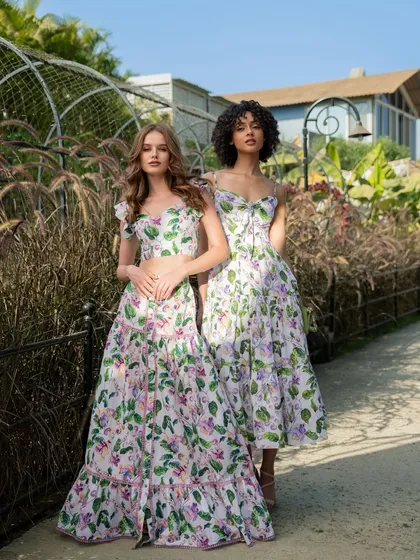 An outdoor campaign image for fashion brand Tangerine Tiger. This shot features two models in complementary floral outfits, set in a lush garden to evoke a fresh, summery feel.