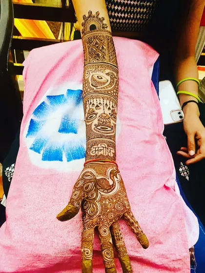 A single arm from a bridal set, featuring the groom's name, a dholki, hanging bells, and a peacock. This is a great example of combining multiple elements into one design.