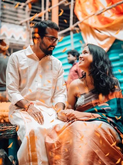 A couple shares a moment amidst the vibrant colors of a flower market. The falling petals add a touch of magic to this candid pre-wedding photograph.