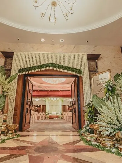 A grand entrance for an indoor wedding, framed with massive arrangements of white tuberoses and woven palm leaves, setting a tone of traditional luxury.