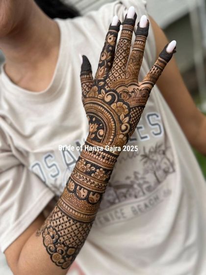 A happy bride showcasing her beautiful back-of-hand mehendi. The design features a central mandala with intricate bands on the arm, creating a look of pure joy and elegance.