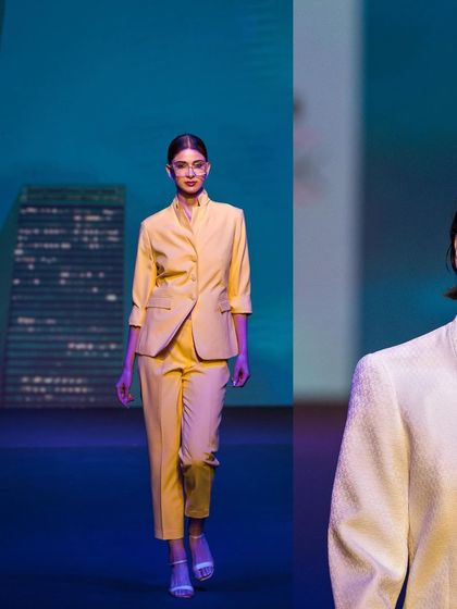 A model walks the runway in a bright yellow pantsuit. The vibrant color pops against the cool-toned background, creating a visually striking image.