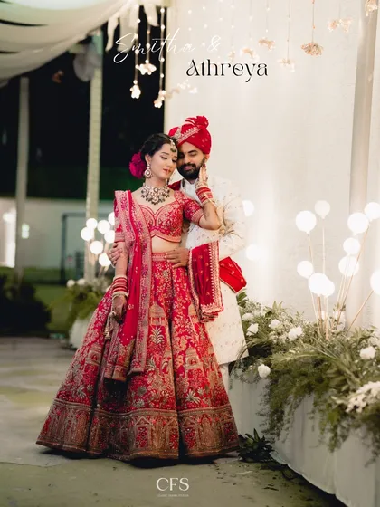 A fairytale moment brought to life. The bride's magnificent red lehenga and the groom's elegant sherwani create a stunning portrait against a backdrop of warm, festive lights, showcasing our expertise in capturing grand North Indian weddings.
