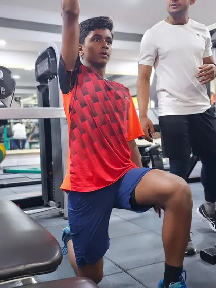 A coach assists a player with a single-arm dumbbell press, an exercise that develops unilateral strength and stability for better racket control.
