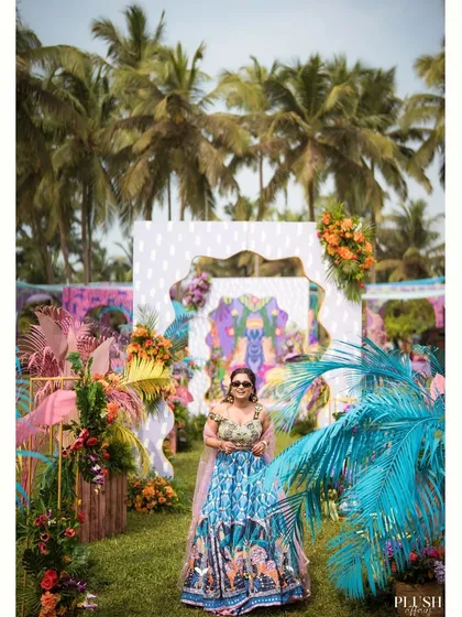 A guest poses against the vibrant, multi-layered photo booth I designed for a carnival-themed Mehendi in Goa. The backdrop includes quirky patterns, colorful florals, and even a flamingo.
