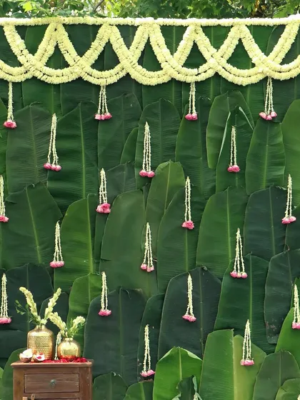 A stunning photo backdrop made entirely of fresh banana leaves, adorned with jasmine and rose garlands, offering a natural and traditional photo opportunity.