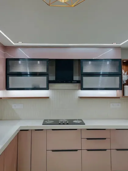 A pretty-in-pink modular kitchen. The rose-gold colored cabinets, white countertops, and stylish black-and-glass overhead units create a chic and modern look.