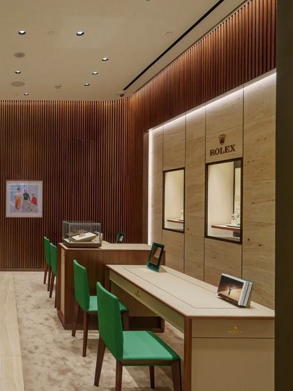 The display and consultation zones in the Rolex store are orchestrated for a seamless customer journey. The clean lines of the counters, paired with the warmth of wood and the richness of green leather chairs, create a balanced and sophisticated retail environment.