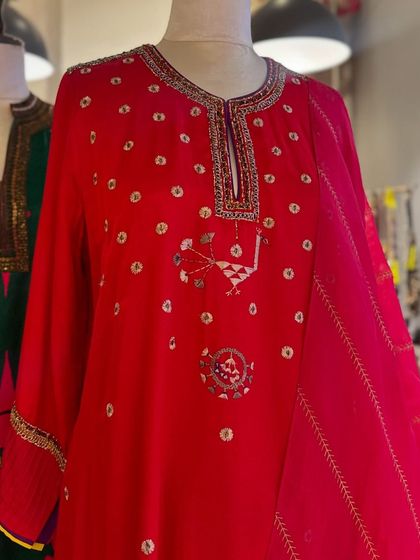 A close-up of a vibrant red kurta with unique, playful embroidery, showcasing a mix of motifs and mirror work.