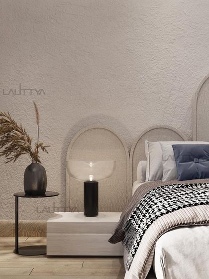 A detail of a modern, minimalist bed design. The neutral-toned headboard with an arched design creates a soft backdrop, complemented by a houndstooth throw and a simple black side table.