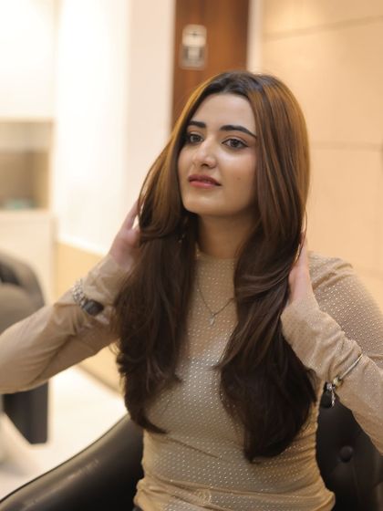 This client is admiring her new light brown color with subtle layers. The shade was chosen to complement her skin tone, and the soft blowout adds volume and showcases the hair's healthy condition.