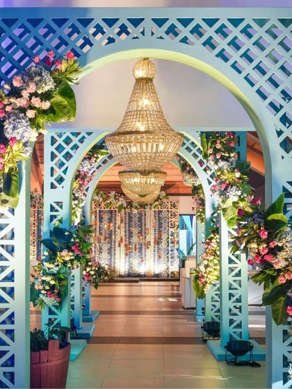 An elegant entranceway with turquoise arches and beautiful floral decorations. The path leads to a grand hall, with chandeliers adding a touch of luxury to the mehendi ceremony.